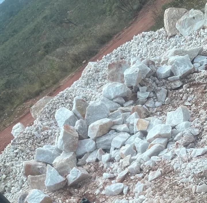 Pilha de quartzo à beira da estrada de terra vermelha que corta a jazida, com a serra ao fundo